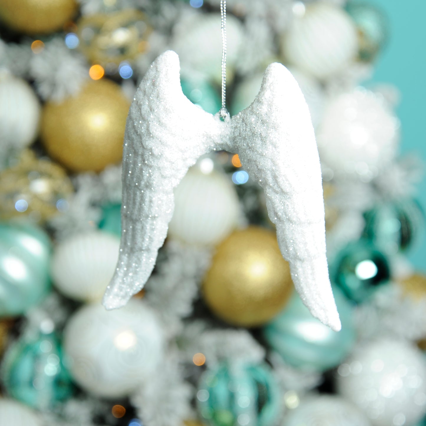 Picture image of hanging white,  glittery angel wings with a gold, white and green bedecked Christmas tree in the background.